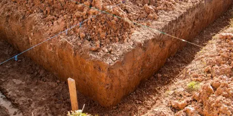 Wyznaczone wykopy pod fundamenty, z widocznymi nićmi wyznaczającymi linie i drewnianym palikiem.