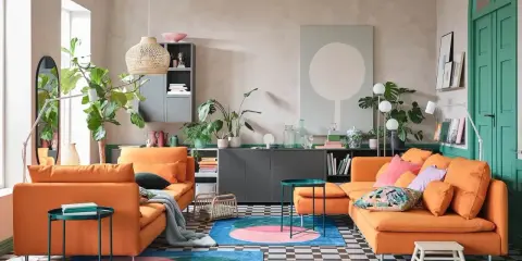Un salon moderne avec deux canapés orange vif. Un tapis rond aux couleurs vives et des plantes vertes apportent de la vie. L'idée est d'associer 2 canapés différents pour un style unique.