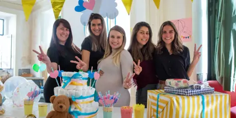 Pięć uśmiechniętych kobiet świętuje baby shower. Na stole tort z pieluch, prezenty i słodkości. To radosne wydarzenie, co to jest baby shower, pełne miłości i oczekiwania.