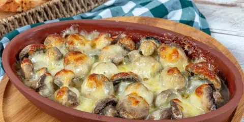 Pieczarki zapiekane z serem w glinianym naczyniu, obok koszyk z pieczywem.
