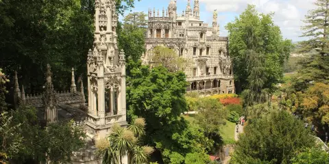 Sintra co zobaczyć: Quinta da Regaleira z wieżą i pałacem, otoczona bujną zielenią i kolorowymi rabatami.