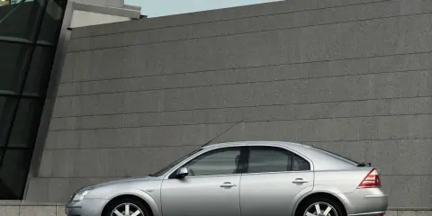 Srebrny Ford Mondeo MK3 2.0 TDCI stoi przed nowoczesnym budynkiem z kamienną fasadą.