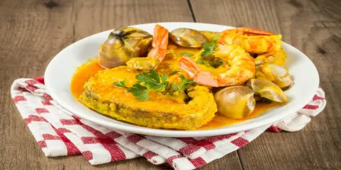 Plato de comida asturiana con un trozo de pescado, gambas y almejas en salsa.