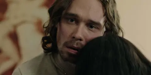 En man med långt hår och blå ögon kramar någon i tv-serien "Knutby".