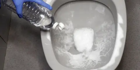 Guante azul vierte líquido de una botella en el inodoro. Solución para saber qué hacer si se atasca el vater.