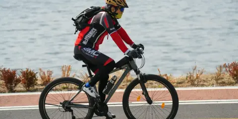 Rowerzysta w kasku i masce jedzie rowerem wzdłuż jeziora. Idealne noclegi dla rowerzystów czekają po wyczerpującej trasie.