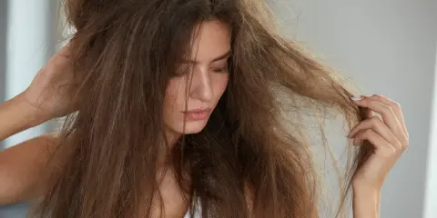 Kobieta zmartwiona swoimi **suchymi końcówkami włosów**, które są splątane i matowe.