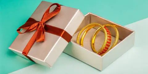 Scatola regalo aperta con bracciali dorati e rossi. Come capire se un bracciale è oro? Osserva la lucentezza e i dettagli.