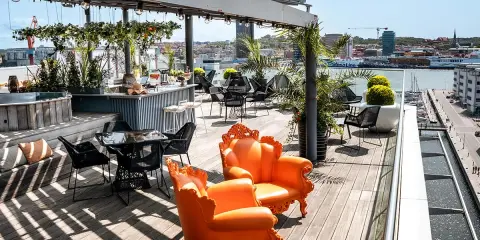 Solig rooftop bar i Göteborg med orangea fåtöljer och utsikt över hamnen.
