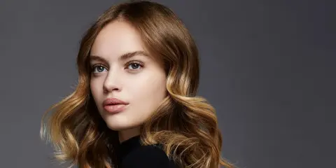 Porträt einer jungen Frau mit welligem, braunem Haar, das mit Balayage-Technik aufgehellt wurde.