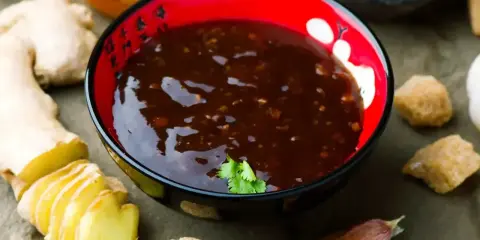 Sos teriyaki przepis: miseczka pełna aromatycznego sosu, obok świeży imbir, czosnek i brązowy cukier. Idealny do dań azjatyckich.