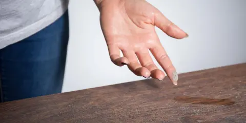 Mano con polvo en los dedos sobre una mesa de madera, mostrando porque sale tanta pelusa en casa.