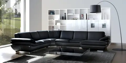 Sofá modular negro de cuero, con mesa de centro de cristal y estanterías blancas. Un diseño de gran dimensión.