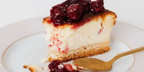 Sernik z obfitym lukrem i frużeliną wiśniową, obok złota łyżeczka.