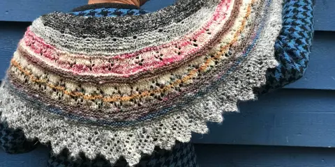 Un chal de lana tejido con hilos de colores, con un intrincado diseño de encaje y bordes festoneados. Los mantoncillos de crochet son una obra de arte.