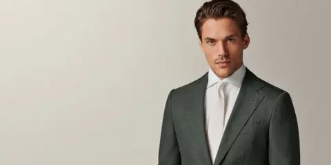 A man in a dark green suit and white shirt with a cream tie. This timeless look embodies the perennial suit meaning of enduring style and sophistication.