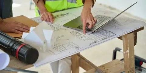 Architectes discutent des plans, pointant du doigt l'emplacement idéal pour installer la VMC dans le modèle de maison.