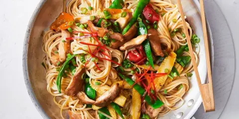 Pyszny makaron sojowy z kurczakiem, warzywami i papryczką chili, podany w metalowej patelni z pałeczkami.