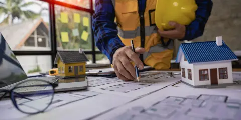 Un architecte examine des plans pour une maison ancienne, évaluant le DPE. Maquettes de maisons sur la table.