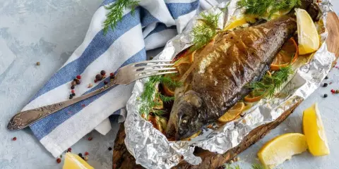 Złocisty pstrąg z piekarnika w folii, pieczony z cytryną i ziołami. Podany na drewnianej desce, gotowy do podania.