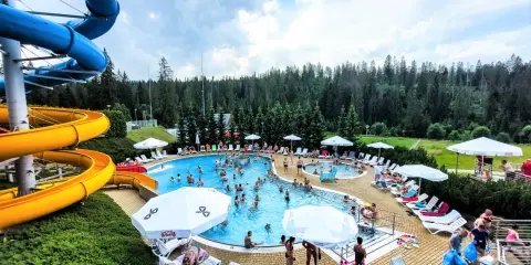 Aqua park Bukowina tętni życiem. Ludzie kąpią się w basenie, zjeżdżają ze zjeżdżalni i odpoczywają na leżakach.