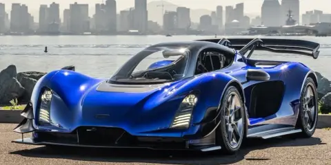 Blauer Ciznger 21c Supersportwagen mit markantem Heckspoiler, vor einer Stadtkulisse am Wasser.