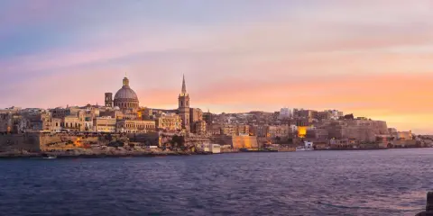 Valletta, Malta, im Dezember bei Sonnenuntergang. Das malerische Malta Wetter im Dezember zeigt sich hier von seiner schönsten Seite, mit warmen Farben am Himmel über der historischen Stadt.