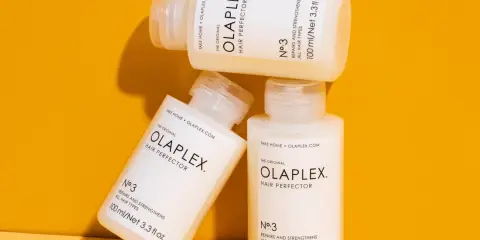 Drei Flaschen der OLAPLEX Serie, "Hair Perfector No.3", liegen übereinander auf einem orangen Hintergrund.