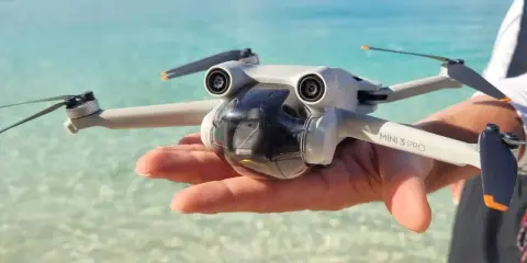 Un drone Mini 3 Pro tenuto in mano su una spiaggia tropicale, pronto per foto droni mozzafiato.
