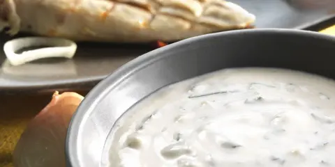 Sauce blanche crémeuse avec herbes, peut-être une différence sauce tartare et béarnaise. Poisson grillé en arrière-plan.