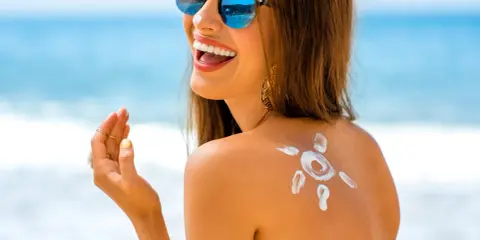 Donna sorridente in spiaggia con crema solare a forma di sole sulla schiena. L'acqua e il sale del mare la aiutano ad abbronzarsi.