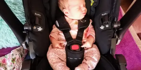 Śpiący noworodek w różowym pajacyku z króliczkami w foteliku Kiddy. Wkładka noworodkowa zapewnia komfort i bezpieczeństwo.