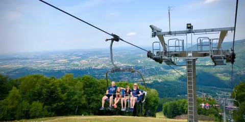 Rodzina na wyciągu krzesełkowym w Wiśle, odkrywająca szlaki turystyczne dla dzieci. Widok na dolinę zapiera dech.