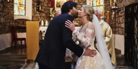 Para młoda całuje się podczas ślubu kościelnego. Panna młoda w pięknej sukni, pan młody w garniturze.
