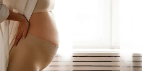 Donna incinta si tiene la schiena, forse per i crampi in gravidanza. Indossa una maglietta e una fascia di supporto.