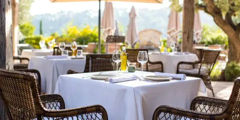 Tables dressées en terrasse, sous un parasol, invitant à savourer une cuisine du terroir authentique. Vins, verres et couverts attendent les convives.