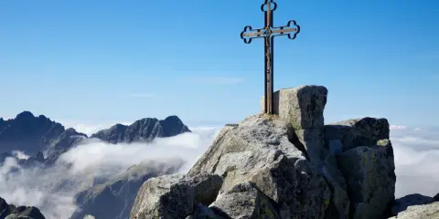 Krzyż na skalistym szczycie, najwyższy szczyt Karpat, góruje nad morzem chmur.