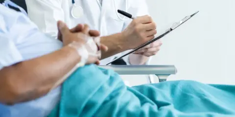 Lekarz notuje na karcie pacjenta, który leży w szpitalu. Rozmowa o pobycie w szpitalu a L4.