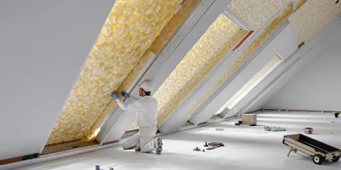 Un ouvrier installe un isolant thermique jaune texturé dans un grenier.