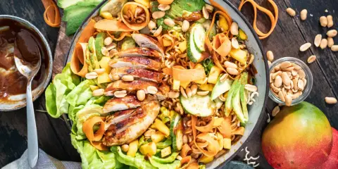 Ein bunter asiatischer Salat mit gegrilltem Hähnchen, Avocado, Mango, Karottenstreifen und Erdnüssen.