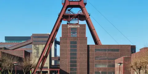 Industrielles Erbe mit rotem Förderturm und Backsteingebäuden. Die Zeche Zollverein strahlt eine starke, urbane Energie aus.
