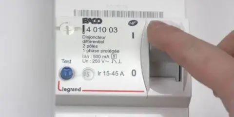Main d'une personne actionnant le levier d'un disjoncteur différentiel Legrand, modèle 15-45 A.