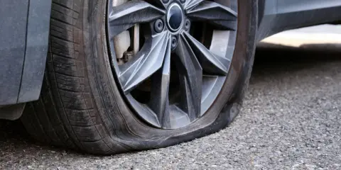 Gomma bucata dell'auto, sgonfia e appoggiata sull'asfalto. Un inconveniente che ferma ogni viaggio.