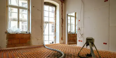 Installation d'un chauffage au sol ancienne génération, avec tuyaux orange et une machine de projection de chape.