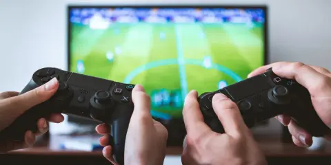 Dwie osoby grają w grę sportową na konsoli. Chcesz wiedzieć, jak zostać testerem gier? Zacznij od grania!