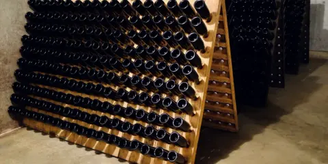 Vinhylla med mörka flaskor, kanske för ett "bereche et fils" vin. Flaskorna står i träställningar i ett källarutrymme.