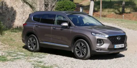 Brązowy Hyundai Santa Fe 2025 na tle kamiennego muru i zieleni.