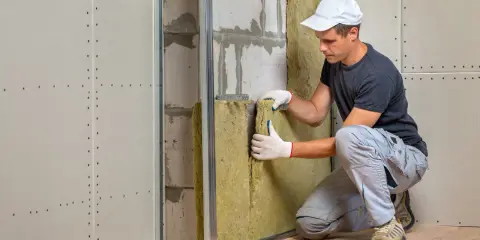 Un ouvrier installe un isolant minéral pour l'isolation mur intérieur. Le chantier progresse.