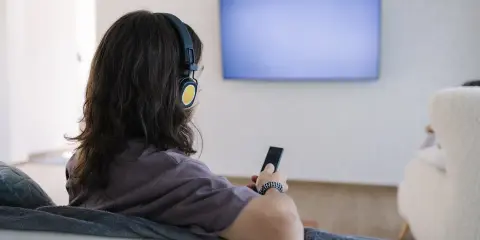 Osoba w słuchawkach z pilotem w ręku, szuka sposobu, jak podłączyć słuchawki bezprzewodowe do telewizora bez bluetooth.