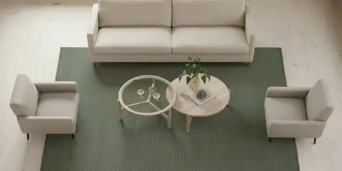 En ljus soffa och två fåtöljer står på en grön matta. Bordet med glas och trä ger en känsla av rymd, och mattans storlek passar perfekt i rummet.